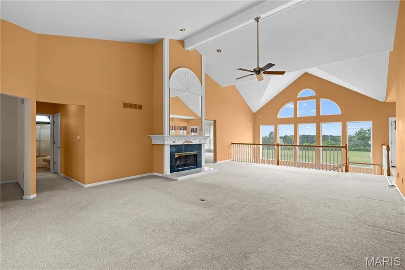 Vaulted ceiling with an exposed beam, fireplace with a decorative mantel and hearth, built-in shelving, large windows, and a ceiling fan — 104 Wolf Trail Court, Defiance, MO 63341
