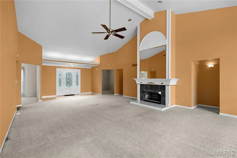 Vaulted ceilings, a built-in fireplace with a mantel, an arched mirror, a front entry door with decorative glass, and a ceiling fan — 104 Wolf Trail Court, Defiance, MO 63341