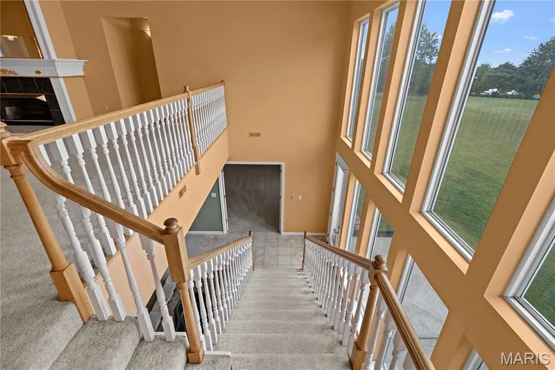 Two-story wall of windows, grand staircase with wood handrails, white balusters, and carpeted treads, and a built-in fireplace with mantel — 104 Wolf Trail Court, Defiance, MO 63341