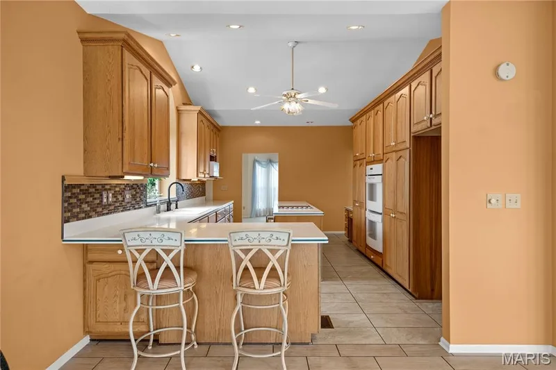 Kitchen featuring extensive wood-finish cabinetry, built-in double ovens, recessed lighting, a ceiling fan, and tile flooring — 104 Wolf Trail Court, Defiance, MO 63341