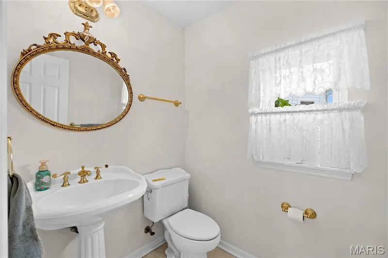 Pedestal sink with brass-finish fixtures, decorative wall mirror, and a window with natural light — 104 Wolf Trail Court, Defiance, MO 63341