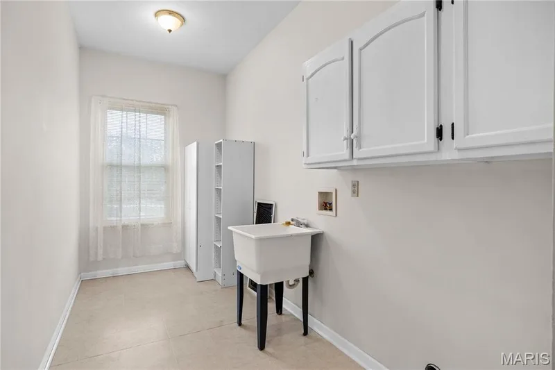 White wall-mounted cabinetry, utility sink, window, and overhead flush-mount light fixture — 104 Wolf Trail Court, Defiance, MO 63341