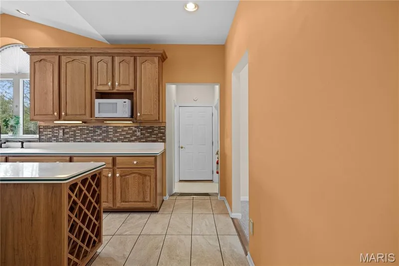 Kitchen featuring wood cabinetry, solid surface countertops, mosaic tile backsplash, and tile flooring — 104 Wolf Trail Court, Defiance, MO 63341