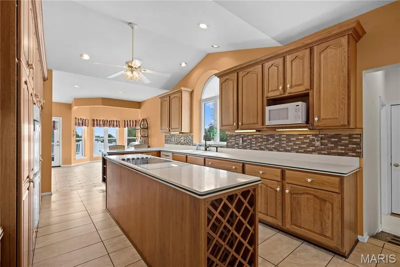 Kitchen featuring wood cabinetry, an island with integrated wine storage, tile flooring, and vaulted ceilings with recessed lighting — 104 Wolf Trail Court, Defiance, MO 63341