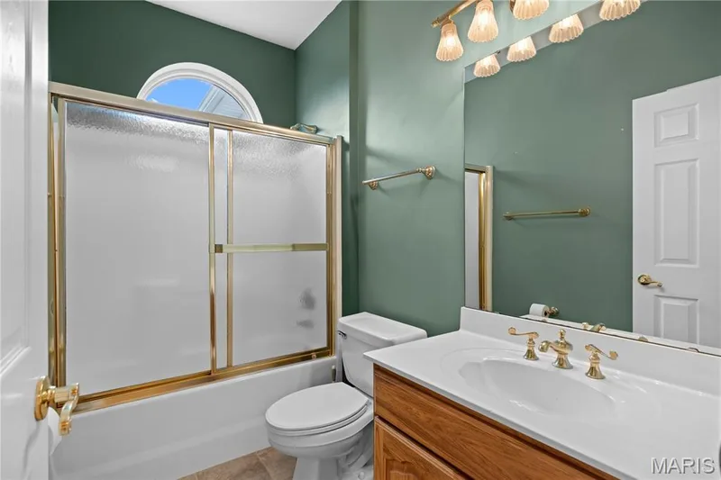Bathroom featuring a tub with sliding shower doors, an arched transom window, a vanity with a white countertop and integrated sink, and a gold-toned faucet — 104 Wolf Trail Court, Defiance, MO 63341