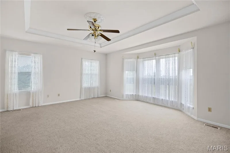 Tray ceiling with decorative ceiling fan, bay window, and neutral carpeting — 104 Wolf Trail Court, Defiance, MO 63341