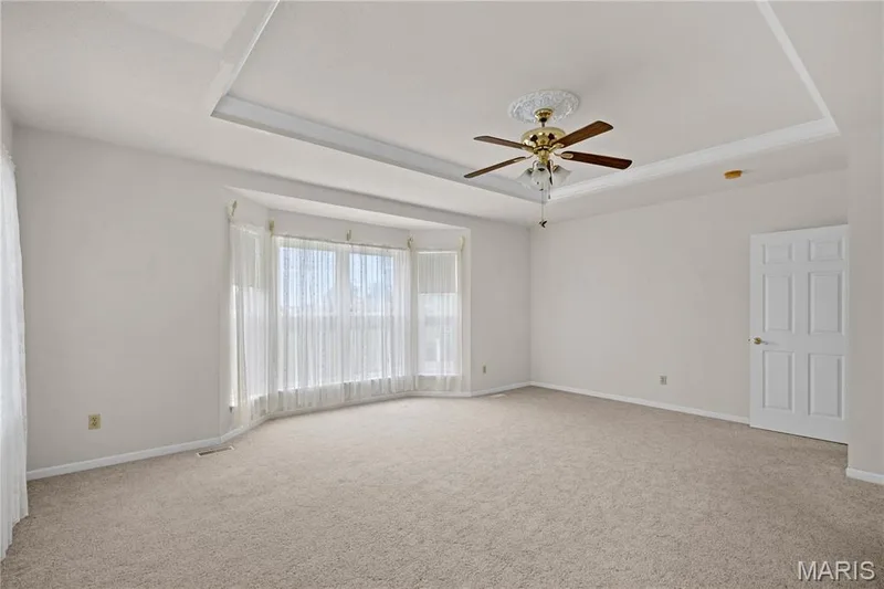 Recessed tray ceiling with crown molding, ceiling fan with light fixture, bay window, light-colored carpeting, and a paneled door — 104 Wolf Trail Court, Defiance, MO 63341
