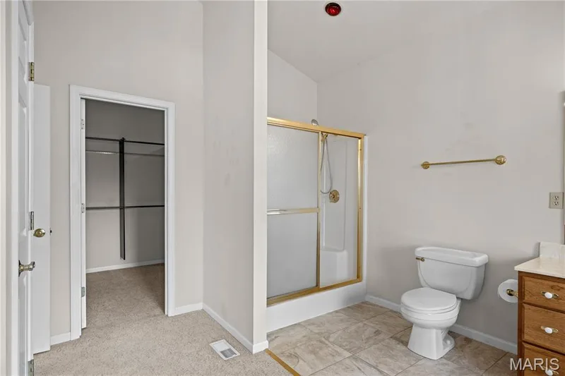Gold-finish framed shower, white toilet, single vanity with wood-finish cabinetry, and built-in closet shelving — 104 Wolf Trail Court, Defiance, MO 63341