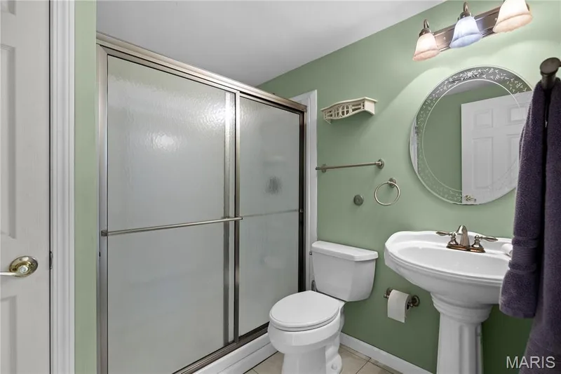 Pedestal sink with brushed nickel faucet, circular mirror, and a three-light vanity fixture — 104 Wolf Trail Court, Defiance, MO 63341