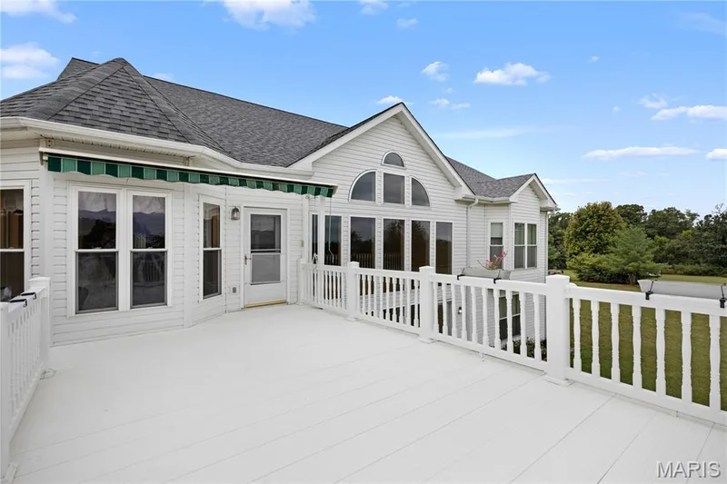 Expansive white deck with white railings, featuring multiple windows, a screened door, and a retractable green awning — 104 Wolf Trail Court, Defiance, MO 63341
