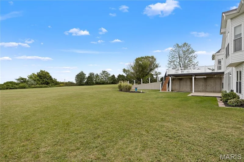 Expansive lawn and a two-story exterior with a raised deck, lower-level patio, and surrounding landscaping — 104 Wolf Trail Court, Defiance, MO 63341