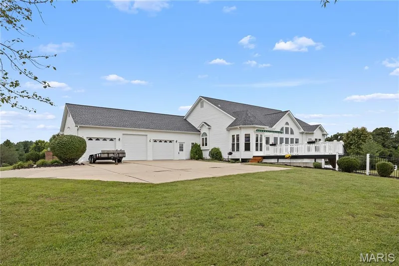 White exterior with a multi-car garage, expansive concrete driveway, and a spacious rear deck — 104 Wolf Trail Court, Defiance, MO 63341