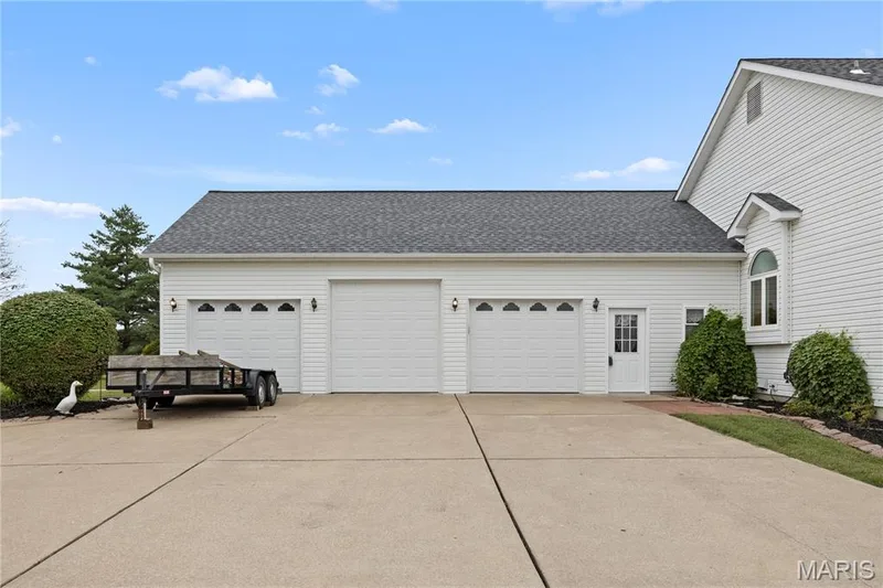 Three-car garage with white paneled doors, exterior lighting, and a separate service door — 104 Wolf Trail Court, Defiance, MO 63341