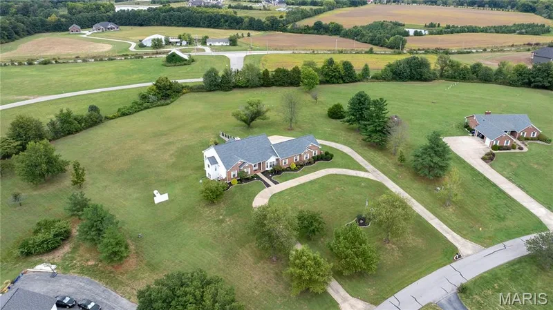 Expansive green landscape featuring two brick residences with dark roofs, mature trees, and paved driveways — 104 Wolf Trail Court, Defiance, MO 63341