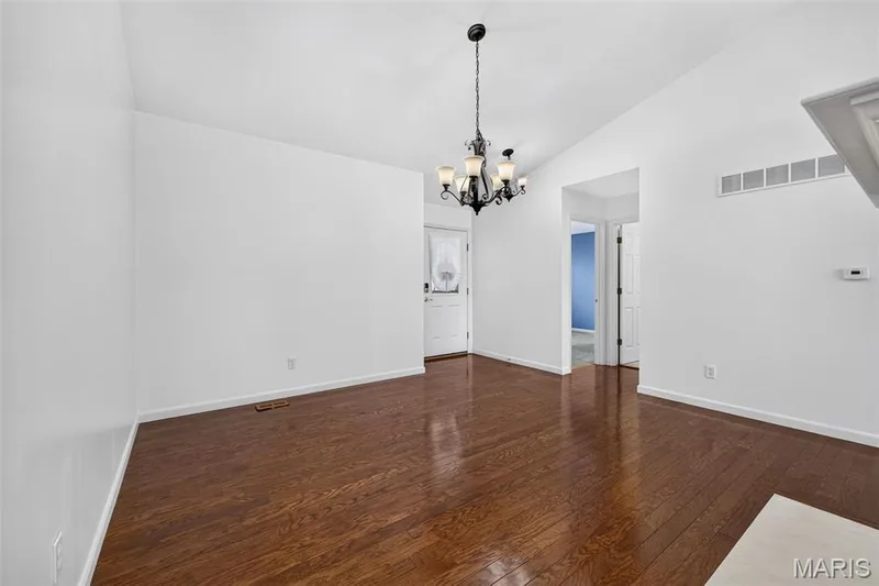 Vaulted ceiling with an ornate chandelier, dark wood-finish flooring, and white painted walls — 20 Autumn Ridge Drive #83B, O'Fallon, MO 63366