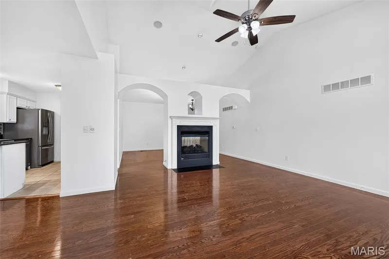 Hardwood-finish flooring throughout, a vaulted ceiling with a ceiling fan, a fireplace with a white mantel, and arched wall openings — 20 Autumn Ridge Drive #83B, O'Fallon, MO 63366