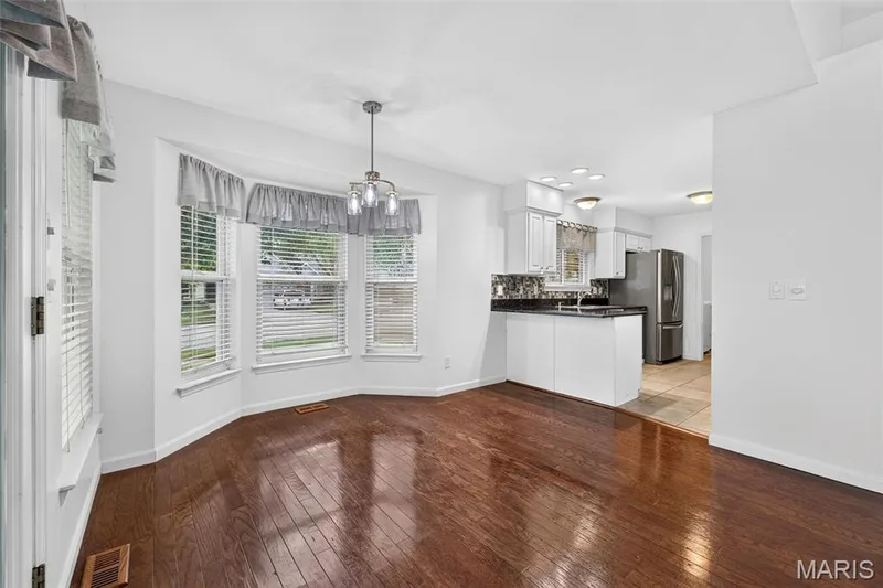 Expansive wood-finish flooring, bay window with multiple panes, modern chandelier, white cabinetry, and a full-size stainless steel refrigerator — 20 Autumn Ridge Drive #83B, O'Fallon, MO 63366