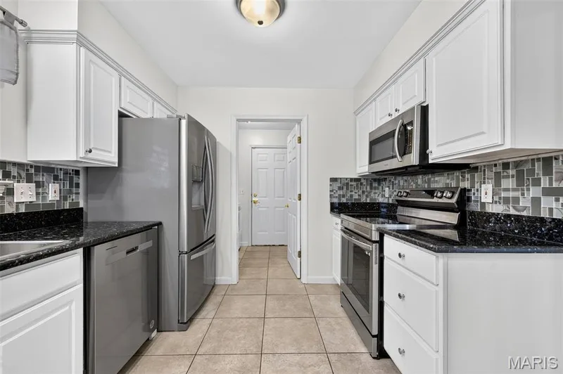 Kitchen featuring stainless steel appliances, white cabinetry, dark speckled countertops, and a mosaic tile backsplash — 20 Autumn Ridge Drive #83B, O'Fallon, MO 63366