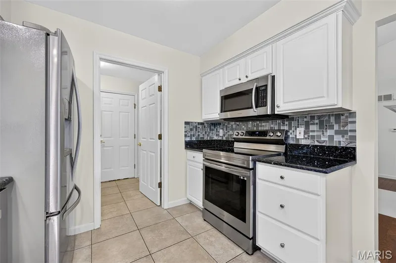 White cabinetry with crown molding, stainless steel appliances, dark stone countertops, tile backsplash, and tile flooring — 20 Autumn Ridge Drive #83B, O'Fallon, MO 63366