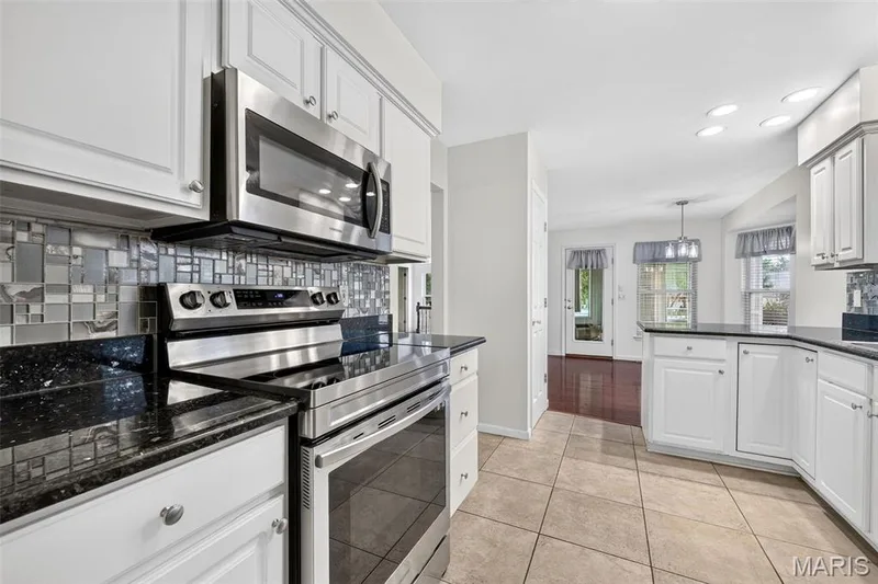 Kitchen featuring white cabinetry, stainless steel appliances, dark countertops, a mosaic tile backsplash, and tile flooring — 20 Autumn Ridge Drive #83B, O'Fallon, MO 63366