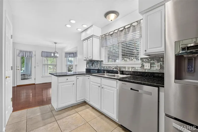 Kitchen featuring white cabinetry, dark countertops, a tile backsplash, stainless steel appliances, and tile flooring — 20 Autumn Ridge Drive #83B, O'Fallon, MO 63366