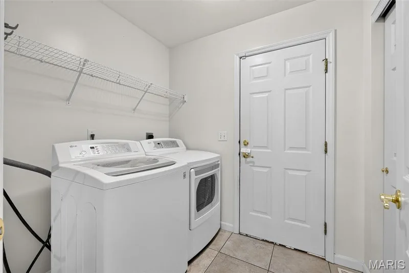 Laundry area featuring tile flooring, white walls, and a white paneled door with brass hardware — 20 Autumn Ridge Drive #83B, O'Fallon, MO 63366
