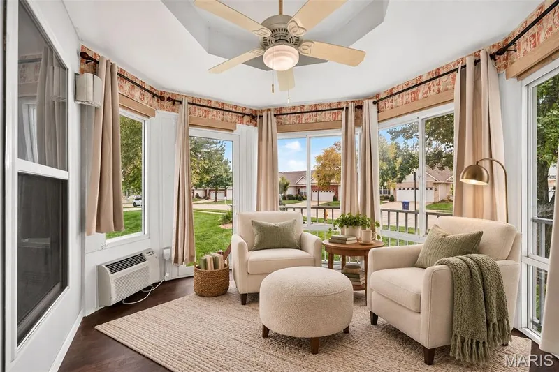 Sunroom featuring expansive windows, dark wood-finish flooring, a tray ceiling with a ceiling fan, and a wall-mounted heating/cooling unit — 20 Autumn Ridge Drive #83B, O'Fallon, MO 63366