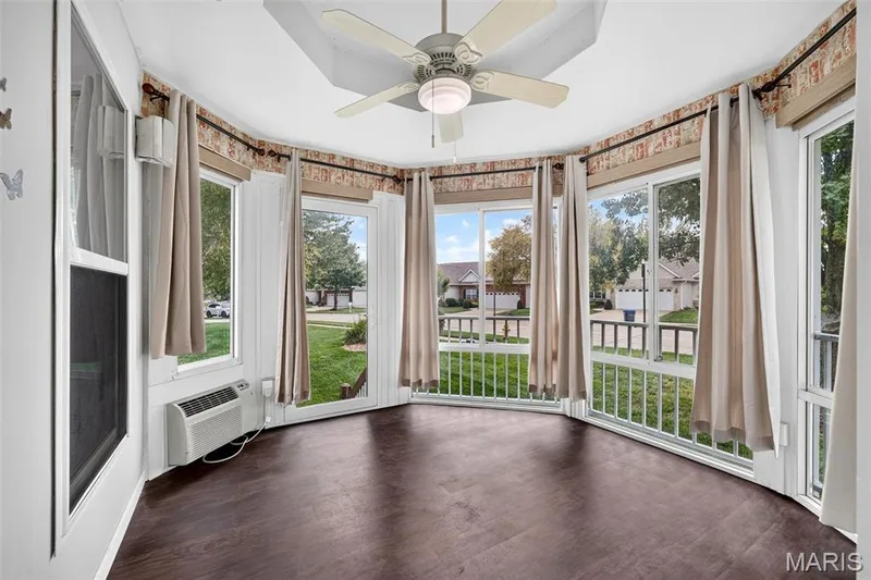 Curved sunroom featuring a ceiling fan, dark wood-finish flooring, multiple windows, and a wall-mounted air conditioning unit — 20 Autumn Ridge Drive #83B, O'Fallon, MO 63366