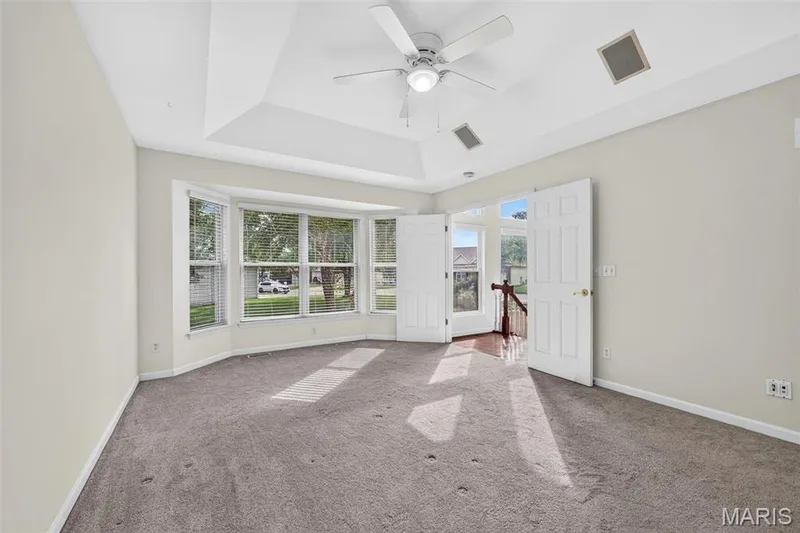 Tray ceiling with a ceiling fan, bay windows with blinds, and white paneled double doors — 20 Autumn Ridge Drive #83B, O'Fallon, MO 63366