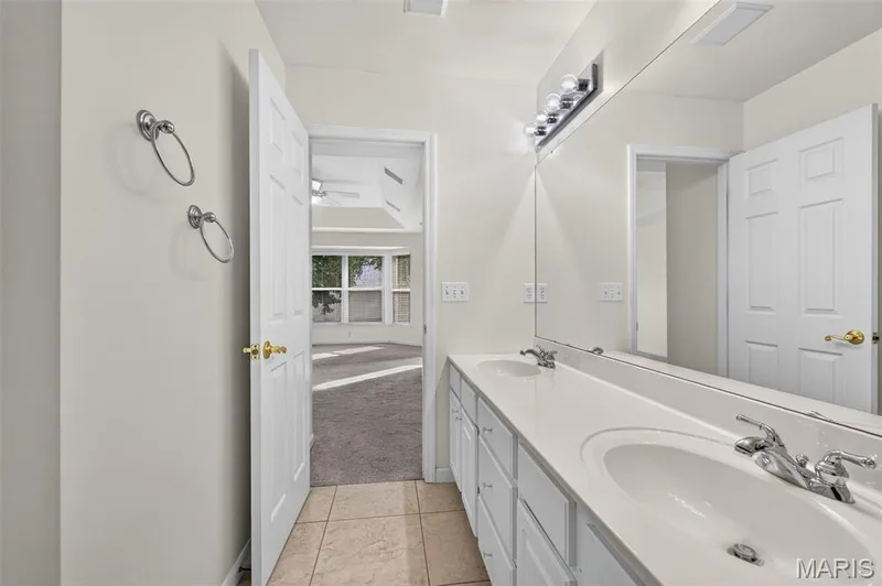 Double vanity with integrated sinks, expansive mirror, wall-mounted light fixture, and tile flooring — 20 Autumn Ridge Drive #83B, O'Fallon, MO 63366