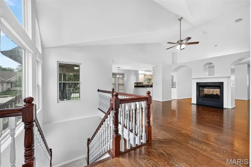 Vaulted ceilings with a ceiling fan, a fireplace with a white mantel, hardwood flooring, an arched entryway, and a staircase with wood banisters — 20 Autumn Ridge Drive #83B, O'Fallon, MO 63366
