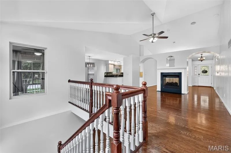 Hardwood flooring, vaulted ceiling, built-in fireplace, decorative archways, and a classic wood and white baluster staircase — 20 Autumn Ridge Drive #83B, O'Fallon, MO 63366