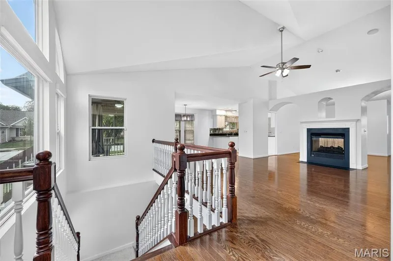 Vaulted ceilings, hardwood flooring, an elegant gas fireplace, a ceiling fan, and a wood staircase with white balusters — 20 Autumn Ridge Drive #83B, O'Fallon, MO 63366