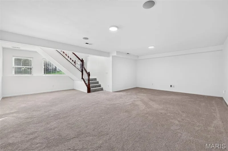 Expansive room with neutral carpeting, recessed lighting, and a staircase featuring a wood handrail and balusters — 20 Autumn Ridge Drive #83B, O'Fallon, MO 63366