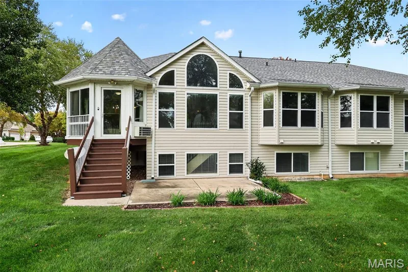 Expansive rear exterior with light-toned siding, multiple bay windows, a large arched window, a private deck with stairs, and a concrete patio — 20 Autumn Ridge Drive #83B, O'Fallon, MO 63366