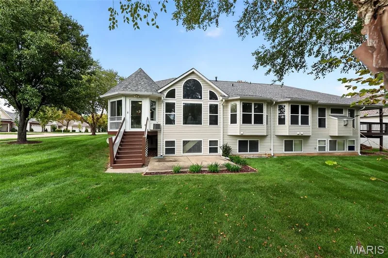 Expansive rear exterior featuring a screened-in porch with a conical roof, large arched window, multiple bay windows, and a ground-level patio — 20 Autumn Ridge Drive #83B, O'Fallon, MO 63366