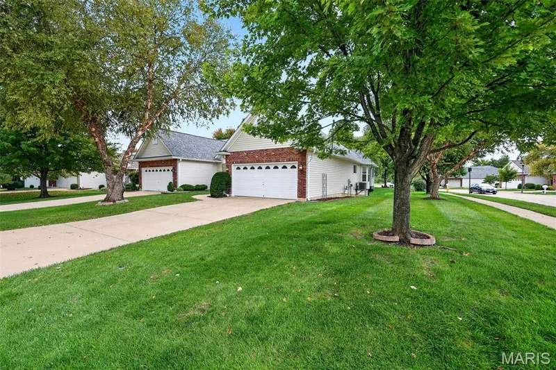 Brick and siding exterior, attached garage, concrete driveway, lush lawn, and mature trees — 20 Autumn Ridge Drive #83B, O'Fallon, MO 63366