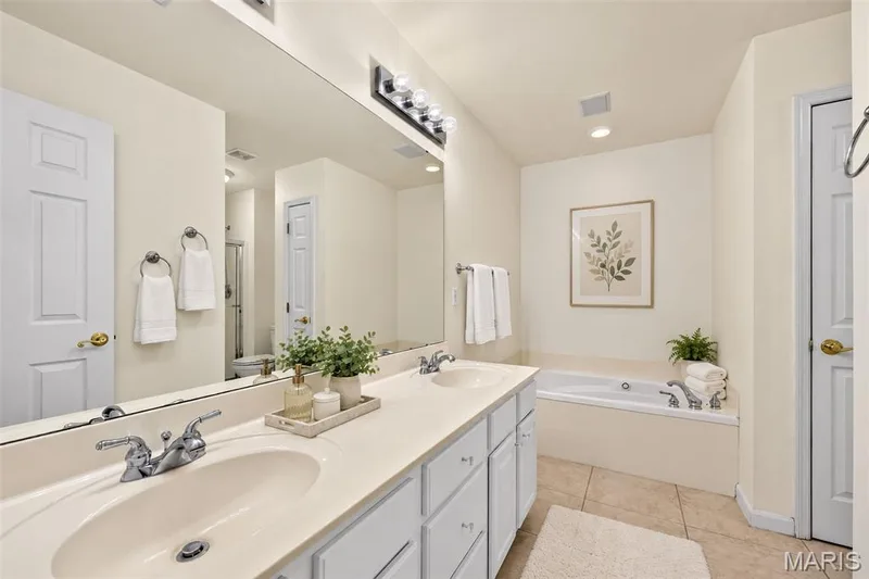 Dual vanity with chrome fixtures and integrated sinks, large wall-mounted mirror, built-in bathtub, light-toned tile flooring, and recessed lighting — 20 Autumn Ridge Drive #83B, O'Fallon, MO 63366