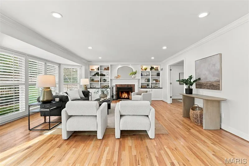 Hardwood flooring extending throughout, bay windows with plantation shutters, recessed lighting, and a fireplace with a brick surround and built-in shelving — 2785 Sun Meadow Drive, Wildwood, MO 63005