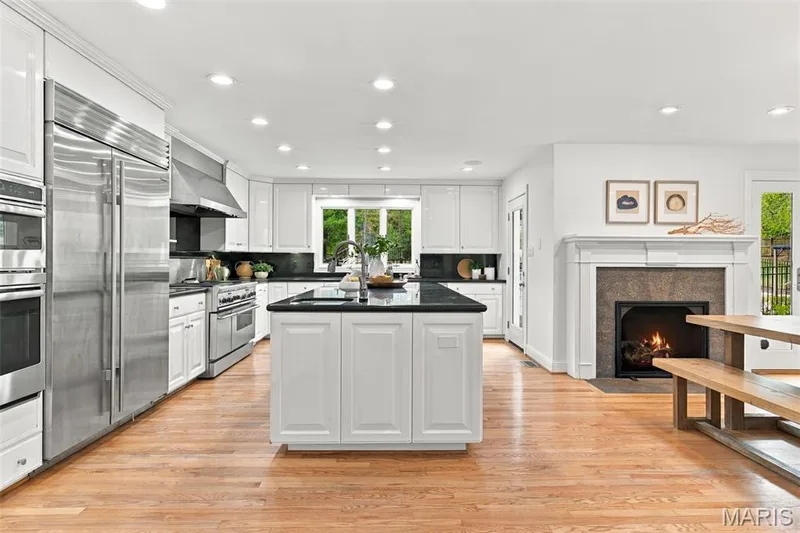 Spacious kitchen featuring white cabinetry, dark countertops, stainless steel appliances, and wood-finish flooring — 2785 Sun Meadow Drive, Wildwood, MO 63005
