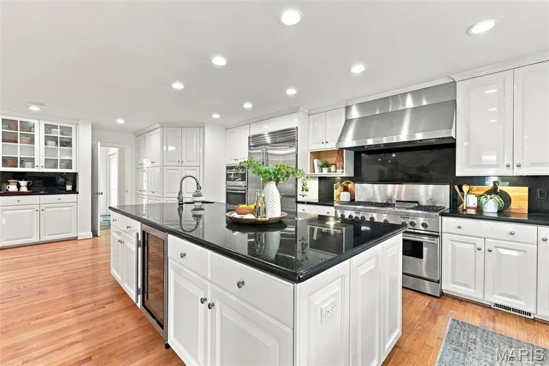 Kitchen featuring an expansive center island with an integrated beverage cooler, stainless steel appliances including a professional-grade range with a substantial hood, white cabinetry, and dark countertops — 2785 Sun Meadow Drive, Wildwood, MO 63005