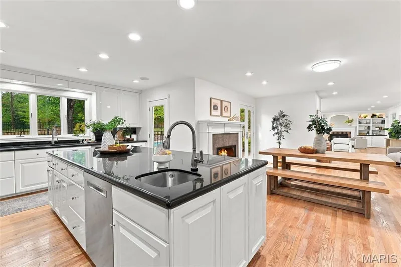 Spacious kitchen featuring an expansive center island with an undermount sink, white cabinetry, integrated stainless steel appliances, and wood-finish flooring — 2785 Sun Meadow Drive, Wildwood, MO 63005