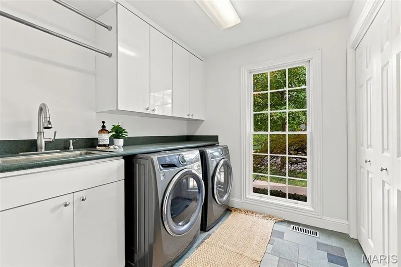 White cabinetry with chrome hardware, dark countertop, stainless steel sink with gooseneck faucet, window with divided lites, and bi-fold doors — 2785 Sun Meadow Drive, Wildwood, MO 63005