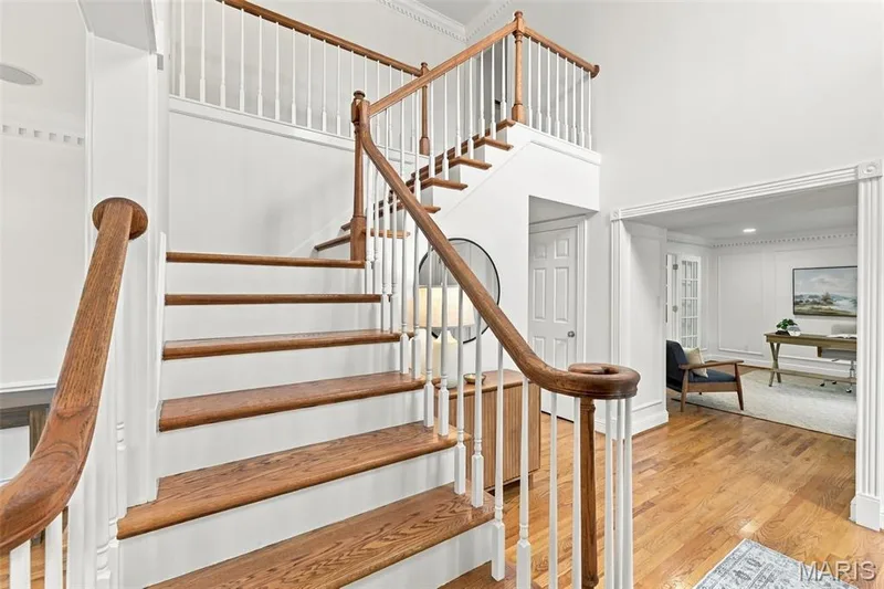 Two-story foyer featuring hardwood flooring, a grand staircase with wood newel posts and railings, white balusters, and crown molding — 2785 Sun Meadow Drive, Wildwood, MO 63005
