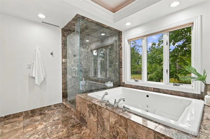 Spacious bathroom featuring a built-in soaking tub, glass-enclosed shower, and large multi-pane window — 2785 Sun Meadow Drive, Wildwood, MO 63005