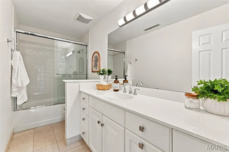White shaker cabinetry with square hardware, large vanity mirror, built-in light fixture, single basin sink, and a combination tub/shower with sliding glass doors — 2785 Sun Meadow Drive, Wildwood, MO 63005
