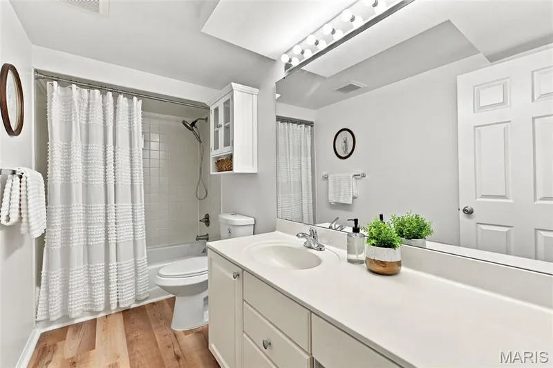 Bathroom featuring wood-finish flooring, a white vanity with integrated sink, a full-width mirror, and a shower-over-tub combination with tile surround — 2785 Sun Meadow Drive, Wildwood, MO 63005