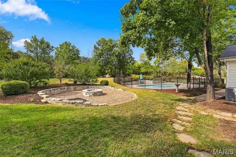 Expansive backyard featuring a stone fire pit, an in-ground pool, and mature trees — 2785 Sun Meadow Drive, Wildwood, MO 63005