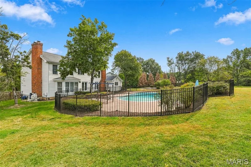 Expansive lawn area featuring a fenced in-ground swimming pool, mature perimeter trees, and a two-story residence with brick chimneys — 2785 Sun Meadow Drive, Wildwood, MO 63005