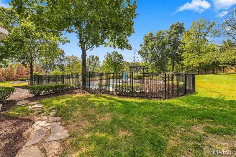 Expansive outdoor area featuring a swimming pool, black metal fencing, stone pathway, and mature trees — 2785 Sun Meadow Drive, Wildwood, MO 63005